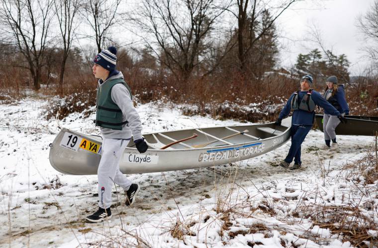 Clayde and Shawn Thompson carry their canoe through the snow to the starting line, with Leslie Voyer following behind, during the 60th annual River Rat Race in Athol on Saturday.