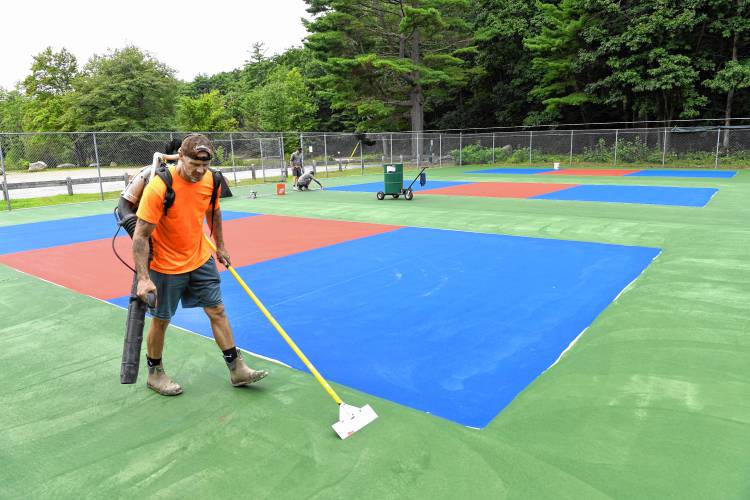 Adam Costa of MA Sealcoating LLC prepares these former tennis courts in Silver Lake Park, which are being converted into three pickleball courts, for a second coat of paint. The project was funded by the Town of Athol, the Athol-Orange Rotary Club and private donations.