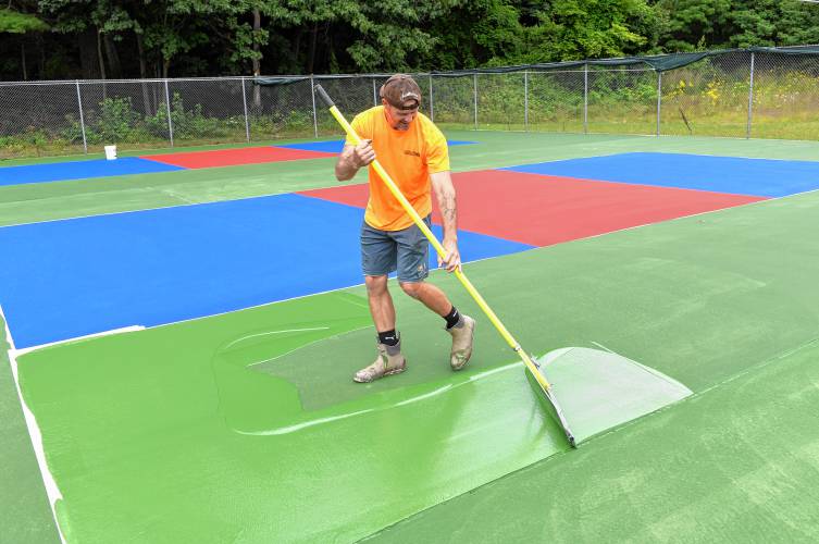 Adam Costa of MA Sealcoating LLC puts a second coat of paint on three pickleball courts that are being created from former tennis courts in Athol’s Silver Lake Park. The project was funded by the Town of Athol, the Athol-Orange Rotary Club and private donations.