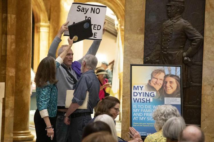 An opponent of medical aid in dying attempts to holds up a sign criticizing the controversial policy at an event hosted by supporters on Tuesday. 