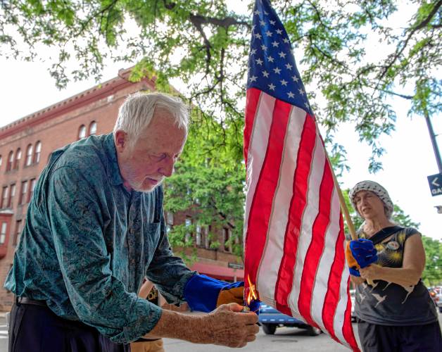 Nick Mottern and Dodi Melnicoff burn an American flag in front of U.S. Rep. Jim McGovern’s Northampton office on Tuesday to protest the government’s complicity in the destruction of Gaza. 