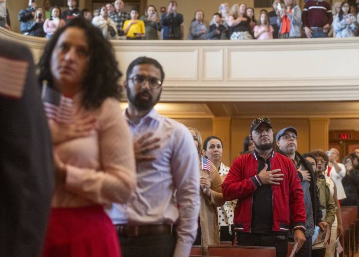 Cruz Aguasvivas, right, originally from the Dominican Republic, recites the Pledge of Allegiance during Tuesday’s naturalization ceremony.