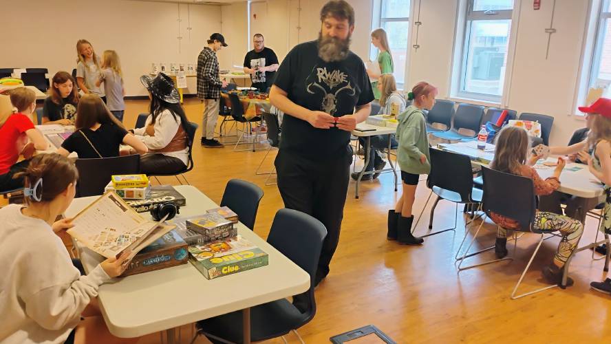 Mini Game Con 2025 organizer Joe McNamara walks through the Athol Public Library's community room, watching attendees playing games both new and old.