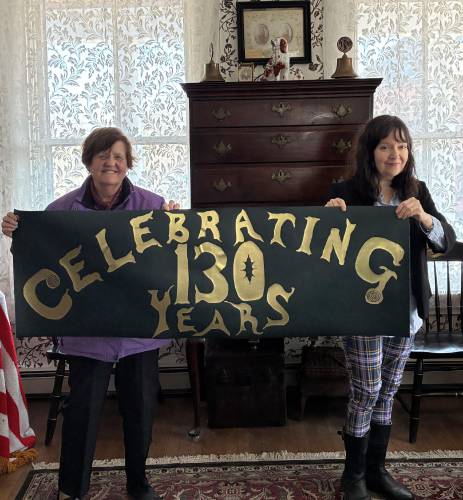 Orange Historical Society President Kathryn Schiappa, left, and Board of Directors member Ann Reed inside the Historical Society parlor with the banner Reed handcrafted and donated for display for the 130th anniversary year of 2025.